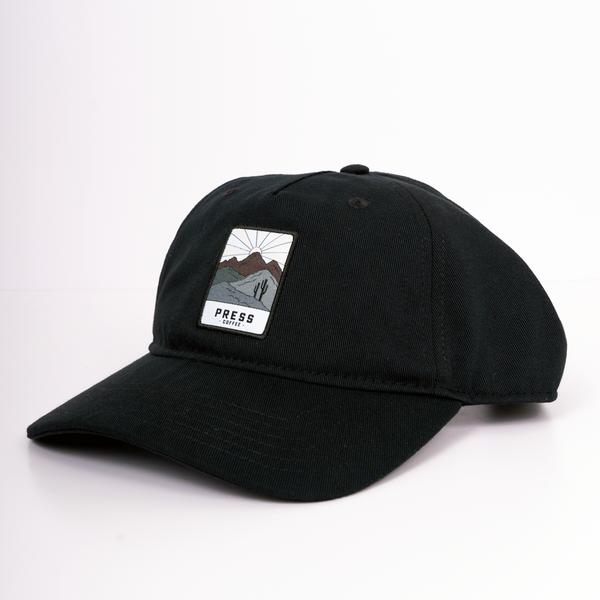 Press Coffee dad hat with a patch that features two cactus, a desert mountain range, and a beaming sun.