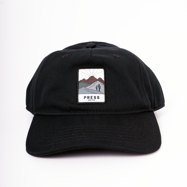 A full view of a Press Coffee dad hat with a patch that features a cactus and desert mountain range.