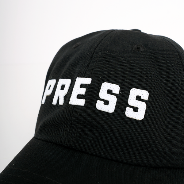 A close up photo of a PRESS dad hat.