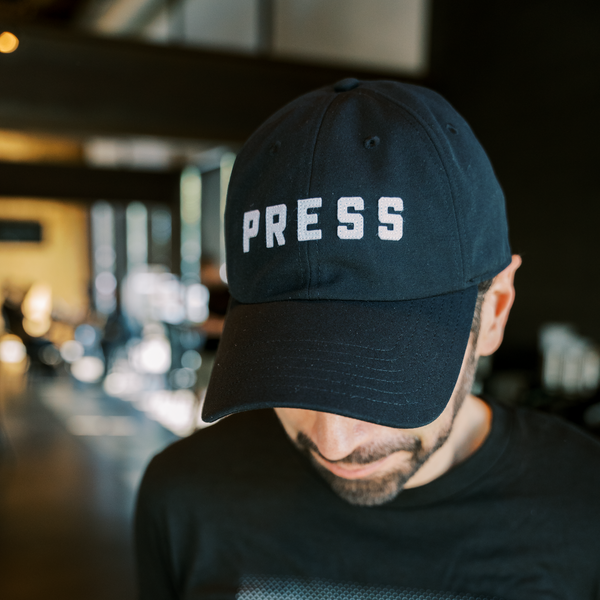 A man with a beard wearing a PRESS dad hat.