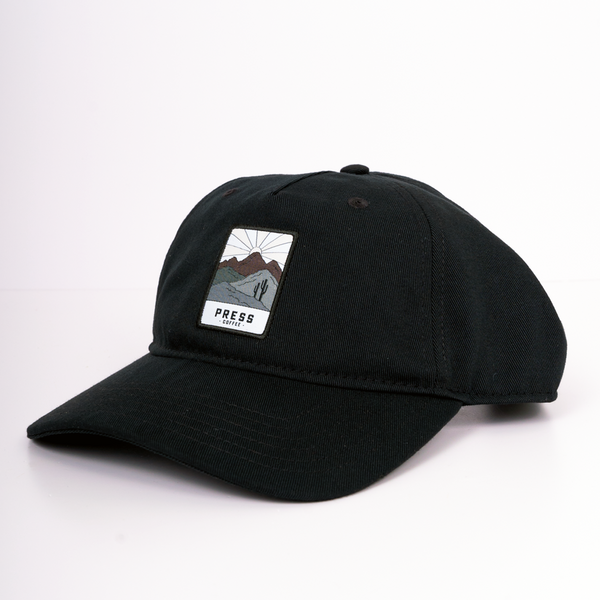 Press Coffee dad hat with a patch that features two cactus, a desert mountain range, and a beaming sun. 