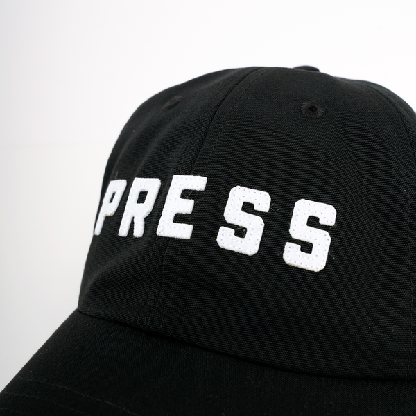 A close up photo of a PRESS dad hat. 