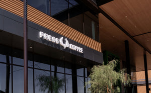 Press Coffee storefront signage mounted on a modern building facade with large glass windows, wood paneling, and a small tree in front.