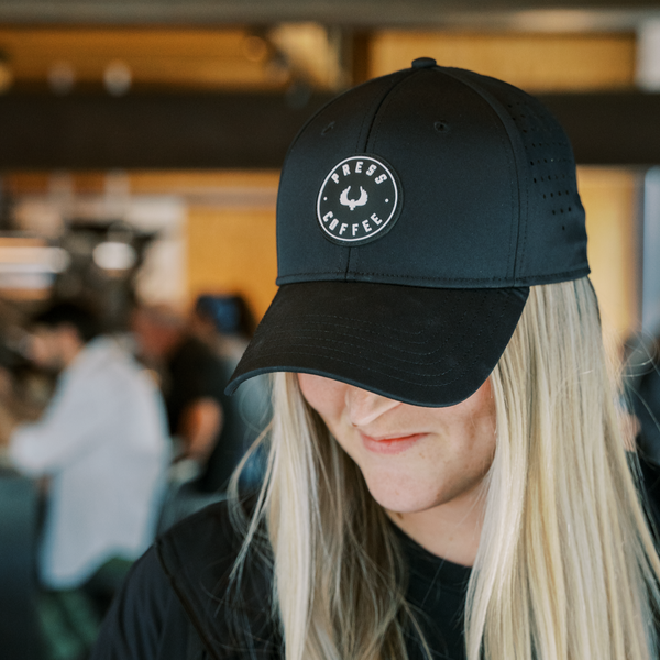 A blonde woman wearing a Press Coffee logo hat while smiling