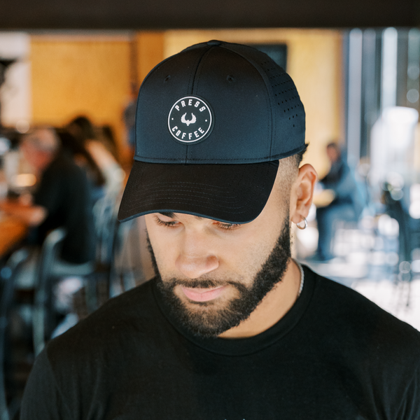 A man with a beard wearing a Press Coffee logo hat. 