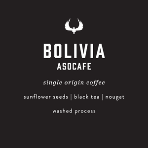 A dark charcoal background with white text reading 'BOLIVIA ASOCAFE' and smaller text below listing ingredients and processing: 'single origin coffee', 'sunflower seeds | black tea | nougat', and 'washed process'. A white winged logo appears above the main text.